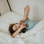 woman covered in white blanket sleeping on white bed comforter