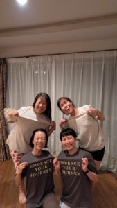 「EMBRACE YOUR JOURNEY」のロゴ入りTシャツを着てピースサインをする4人の女性の集合写真